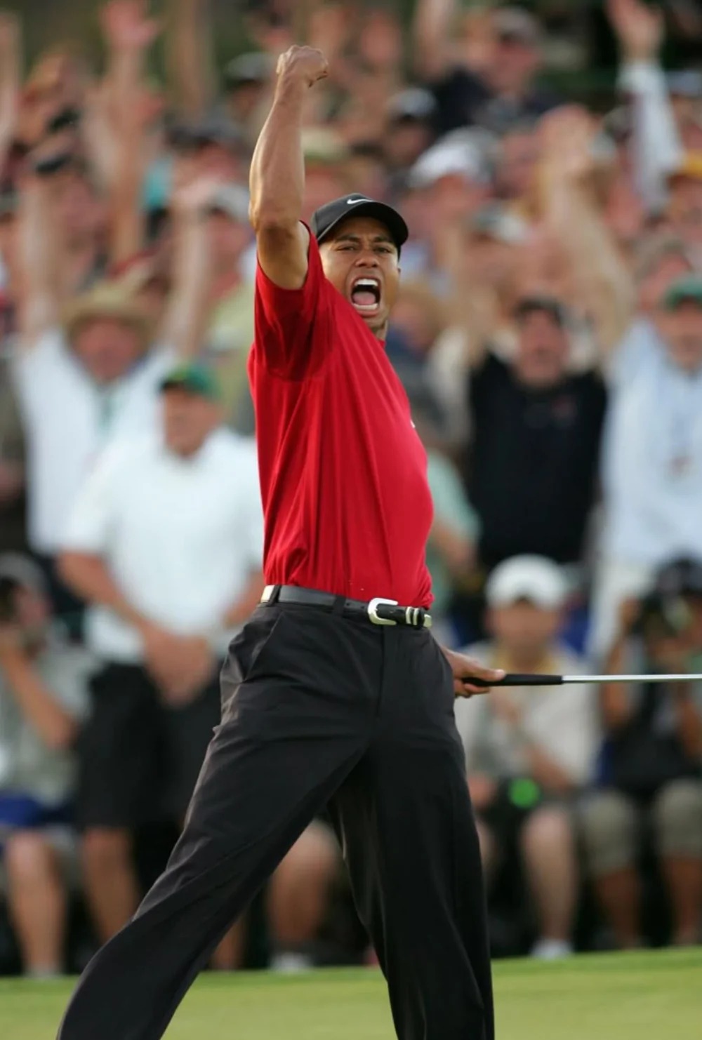 Tiger Woods raising his fist in victory wearing a red shirt on the golf course